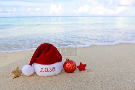 Frohe Weihnachten Hut und Dekoration auf dem weißen karibischen Sand. Hintergrund zum neuen Jahr 2025
