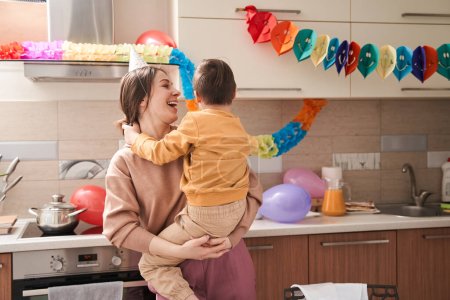 Téléchargez les photos : Taille haute portrait vue de la femme ravie tenant par les mains son enfant mâle avec des troubles génétiques tout en s'amusant à la cuisine - en image libre de droit