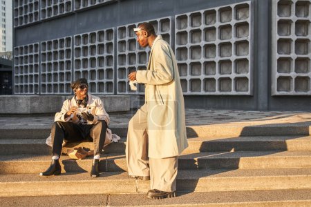 Two multiracial brothers eating fast food and talking with each other while spending time on street stairs. Full length view of the smiling men walking together