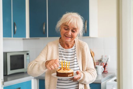 Photo for An elderly woman lighting a candle on a celebratory cake, expressing joy. - Royalty Free Image