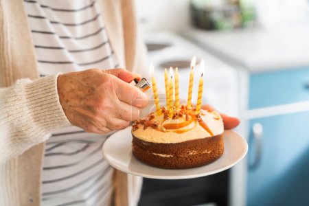 Foto de De cerca una anciana encendiendo una vela en un pastel de celebración, expresando alegría. - Imagen libre de derechos