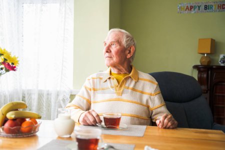 Foto de Feliz anciano en casa, sentado en la mesa y mirando hacia adelante. - Imagen libre de derechos