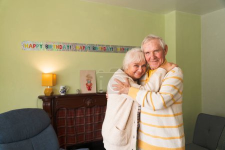 Photo for Happy seniors embrace each other against a birthday celebration backdrop. Concept of elderly longevity at home. - Royalty Free Image