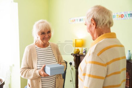 Foto de Una pareja de ancianos intercambiando regalos en el contexto de su casa. Concepto de felices fiestas juntos. - Imagen libre de derechos