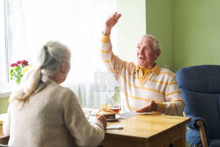 Photo for An elderly couple sitting at home at the table, conversing, morning routine at home. Concept of happy aging together. - Royalty Free Image