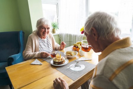 Foto de Una pareja de ancianos sentados en casa a la mesa, conversando, rutina matutina en casa. Concepto de envejecimiento feliz juntos. - Imagen libre de derechos