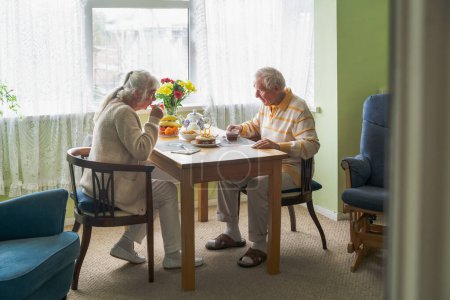Photo for A couple of retirees sitting at a home table celebrating a birthday. - Royalty Free Image