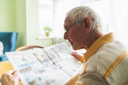 Foto de Un pensionista leyendo prensa fresca en casa, rutina doméstica. Concepto de centenarios. - Imagen libre de derechos