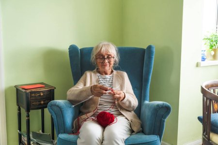 Una anciana, una abuela, se sienta en un sillón y teje con agujas de tejer.