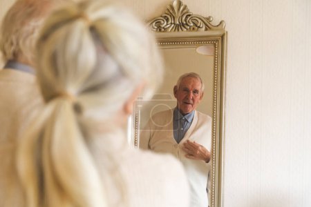 Téléchargez les photos : Couple âgé devant un miroir, la femme ajuste son pull maris, un concept de compagnie durable. - en image libre de droit