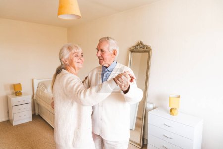 Photo for An elderly couple dancing together in their well-lit room, happy years together. Concept of aging. - Royalty Free Image