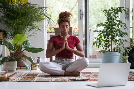 Photo for Serene young woman enjoying meditation in apartment watching online laptop lesson at home. Sport and people lifestyle concept - Royalty Free Image