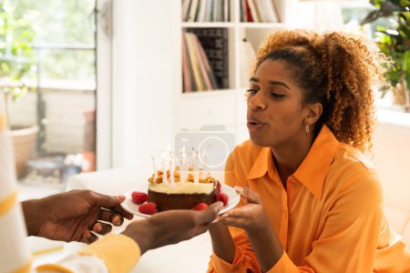 Photo for Cheerful young multiracial married couple celebrate birthday or anniversary with cake. Positive lady blowing candles - Royalty Free Image