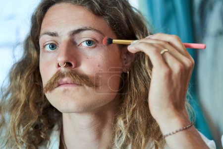 Photo for Portrait of the man visagist with moustaches preparing magnificent makeup and applying eye shadows at home - Royalty Free Image