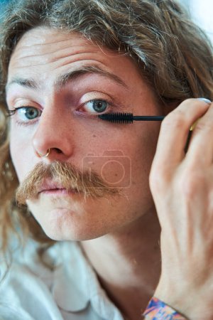 Photo for Portrait of the man visagist with moustaches preparing magnificent makeup and applying mascara at home - Royalty Free Image