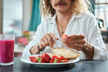 Photo for Cropped view of the moustached man with manicure cutting strawberry and putting it into the croissant while having breakfast - Royalty Free Image