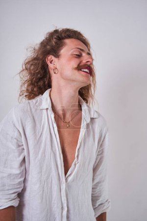Photo for Longhaired man with makeup posing sensually in front of camera at studio. Serious guy looking away during photo shooting - Royalty Free Image