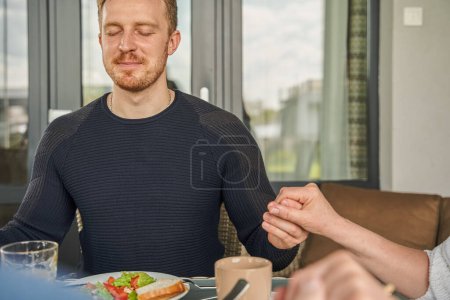 Photo for Cropped view of the christian man praying before breakfast and holding hands at the kitchen table. Religion concept. Stock photo - Royalty Free Image