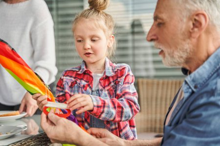 Photo for Little cute girl holding kite and speaking with her grandfather while playing at kitchen. Family relationships concept - Royalty Free Image