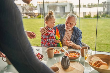 Photo for Serious grandfather playing with his grand daughter while sitting at open air terrace at table. People lifestyle concept - Royalty Free Image