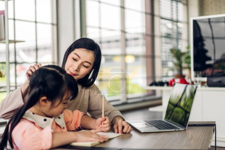 Téléchargez les photos : Portrait heureux amour asiatique famille mère enseigner petite fille asiatique fille apprendre et étudier sur table.Mom et asiatique jeune fille écriture avec livre et crayon faire des leçons à la maison.Éducation - en image libre de droit