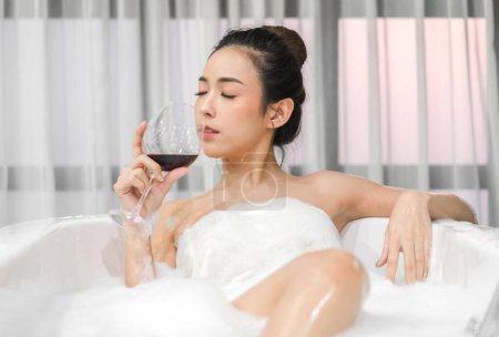 Téléchargez les photos : Portrait de sourire de beauté heureuse jolie femme asiatique propre fraîche et saine soin spa de la peau blanche profiter de détente prendre une douche et bain avec mousse à bulles spa dans la baignoire à la salle de bain - en image libre de droit