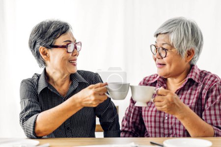 Téléchargez les photos : Portrait de deux amis heureux personnes âgées âgées asiatiques femmes souriantes et parler boire du café à la maison.Concept de retraite - en image libre de droit
