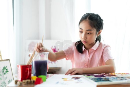 Téléchargez les photos : Petit artiste asiatique fille dessin sur toile avec palette de couleurs et peinture à l'aquarelle à la maison - en image libre de droit