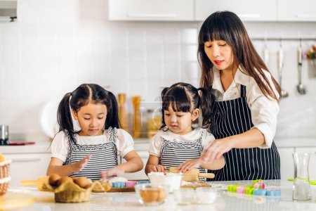 Téléchargez les photos : Portrait de jouir heureux amour asiatique famille mère et petit tout-petit asiatique fille fille enfant avoir plaisir à cuisiner avec de la pâte pour biscuit maison et ingrédient gâteau sur la table dans la cuisine - en image libre de droit