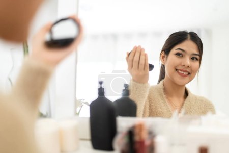 Téléchargez les photos : Sourire de jeune belle belle femme asiatique propre fraîche et saine peau blanche. Fille asiatique tenant brosses de maquillage et maquillage sur le visage avec des cosmétiques fixés à la maison. Beauté faciale - en image libre de droit
