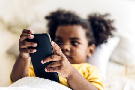 Téléchargez les photos : Portrait de heureuse petite fille afro-américaine enfant en utilisant un smartphone numérique jouer au jeu en ligne et les médias sociaux - en image libre de droit