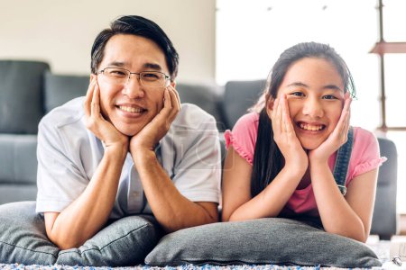 Téléchargez les photos : Portrait profiter heureux sourire amour asiatique famille père et les jeunes parents petite fille asiatique regardant caméra dans les moments de bon temps couché sur le sol à la maison - en image libre de droit