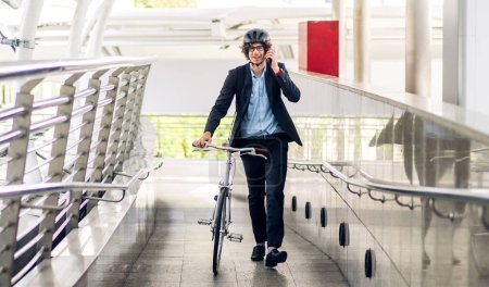 Téléchargez les photos : Portrait décontracté hipster bel homme d'affaires avec sac à dos parler sur smartphone tout en faisant la navette à vélo sur la route de la ville de la rue aller au travail.concept de vélo de transport de voyage d'affaires - en image libre de droit
