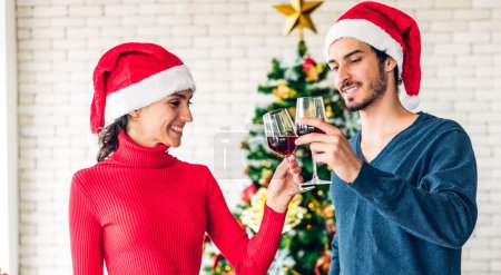 Téléchargez les photos : Romantique doux couple dans chapeaux Santa avoir du plaisir et boire des verres à vin tout en célébrant la veille du Nouvel An et profiter de passer du temps ensemble dans le temps de Noël à la maison - en image libre de droit