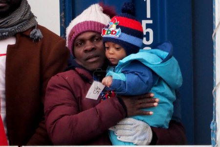 Foto de Migrante con un niño en brazos espera para salir de la nave. El barco de rescate alemán "Sea-Eye 4" llega al puerto de Nápoles con 109 migrantes a bordo, incluidos 35 menores de edad, 18 mujeres, una de las cuales está embarazada y dos fallecidas.. - Imagen libre de derechos