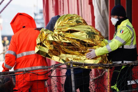Foto de Migrante sale del barco acompañado de voluntarios de protección civil. El barco de rescate alemán "Sea-Eye 4" llega al puerto de Nápoles con 109 migrantes a bordo, incluidos 35 menores de edad, 18 mujeres, una de las cuales está embarazada y dos fallecidas.. - Imagen libre de derechos