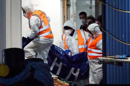Foto de Oficiales de policía mortuorios sacan el cuerpo de un migrante de la nave. El barco de rescate alemán "Sea-Eye 4" llega al puerto de Nápoles con 109 migrantes a bordo, incluidos 35 menores de edad, 18 mujeres, una de las cuales está embarazada y dos fallecidas.. - Imagen libre de derechos