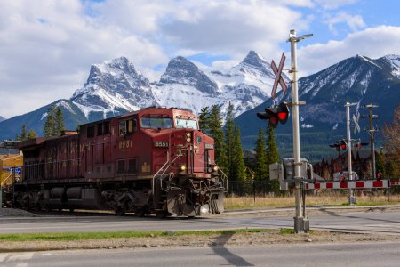 Téléchargez les photos : A Canadian Pacific locomotive at a level-crossing in Canmore, Alberta.  In the background are the Three Sisters... part of the Canadian Rocky Mountains. - en image libre de droit