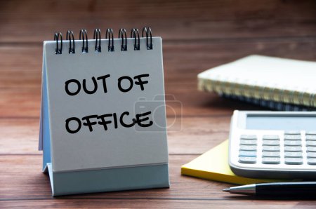 Out of office text on calendar desk with notebook, calculator and pen background. Out of office concept