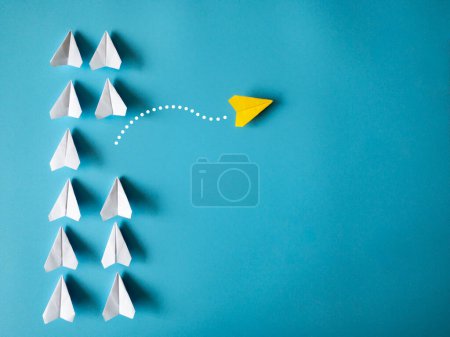 Téléchargez les photos : Yellow paper airplane origami leaving other white airplanes on blue background with customizable space for text. Leadership skills concept. - en image libre de droit