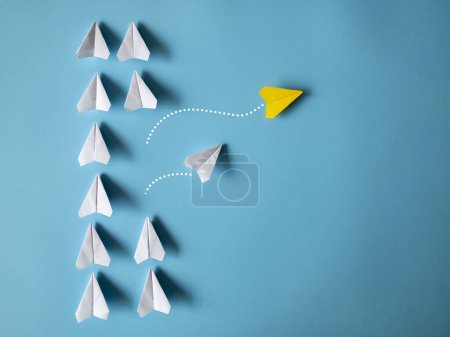 Téléchargez les photos : Yellow and white paper airplanes origami leaving other white airplanes on blue background with customizable space for text. Leadership skills concept. - en image libre de droit