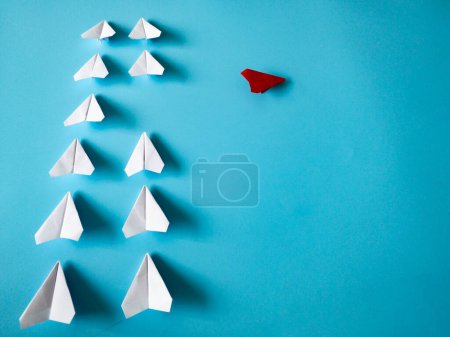 Téléchargez les photos : Red airplane origami leaving other white airplanes on blue background with customizable space for text. Leadership skills concept. - en image libre de droit
