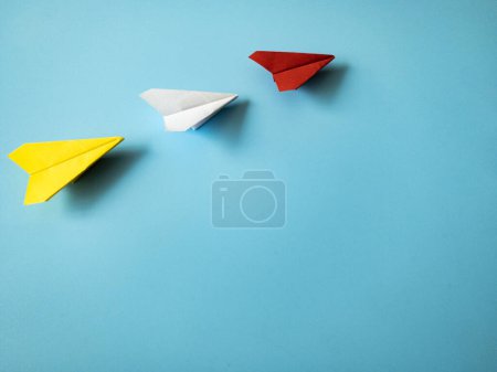 Téléchargez les photos : Red paper airplane origami leading white and yellow airplanes on blue background with customizable space for text. Leadership skills concept - en image libre de droit