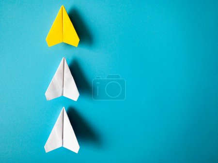 Téléchargez les photos : Yellow paper airplane origami leading white airplanes on blue background with customizable space for text. Leadership skills concept - en image libre de droit