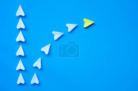 Yellow paper airplane origami leading other white airplanes on blue background with customizable space for text or ideas. Leadership skills concept and copy space.
