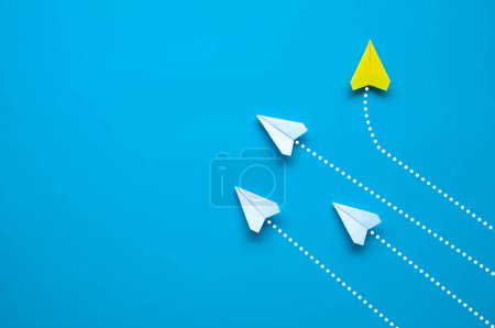 Foto de Vista superior del avión de papel - origami de avión de papel amarillo volando en una dirección diferente dejando otros aviones blancos sobre fondo azul. Concepto de liderazgo. - Imagen libre de derechos