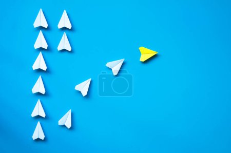 Yellow paper airplane origami leaving with other white airplanes on blue background with customizable space for text or ideas. Leadership skills concept and copy space.