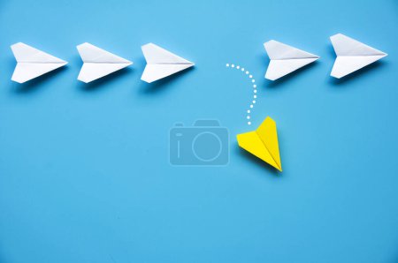 Yellow paper airplane origami leaving other white airplanes on blue background with customizable space for text or ideas. Leadership skills concept and copy space.