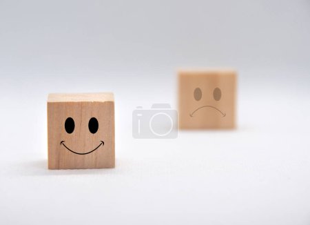 Glückliche und traurige Emoticon-Gesichter auf Holzwürfeln mit weißem Hintergrund. Kundenfeedback, Zufriedenheit und Bewertungskonzept.