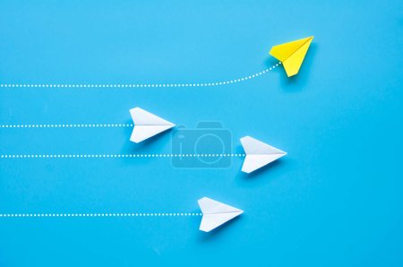Top view of yellow paper airplane origami flying to a different direction leaving other white airplanes on blue background. Leadership and direction concept.